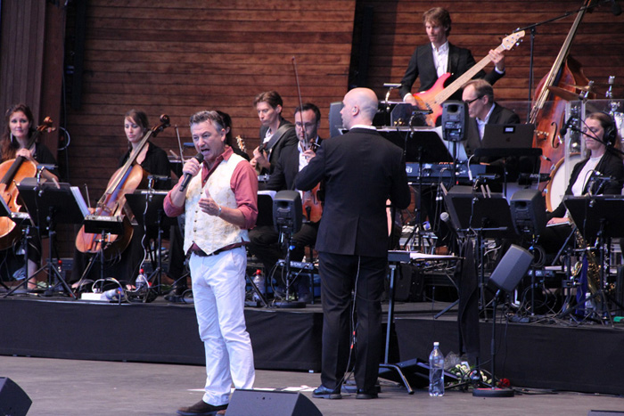 Anders framför orkestern på Sollidenscenen i vita byxor, röd skjorta och guldgul väst.