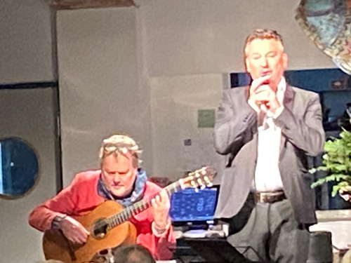 Bengt Magnusson, sittande i ljusröd kavaj,  spelar gitarr. Anders Ekborg, stående bredvid i mörk kostym och vit skjorta, sjunger.