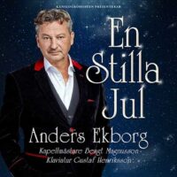 Anders Ekborg i mörk kostym och vit skjorta, mot blå bakgrund. Promotionbild.