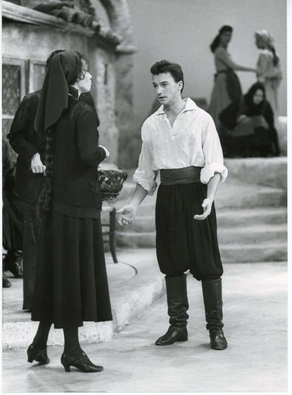 Anders Ekborg på scenen, klädd i vit skjorta och svarta byxor i föreställningen Zorba 1986. Han står mittemot en svartklädd kvinna. i bakgrunden scendekor.